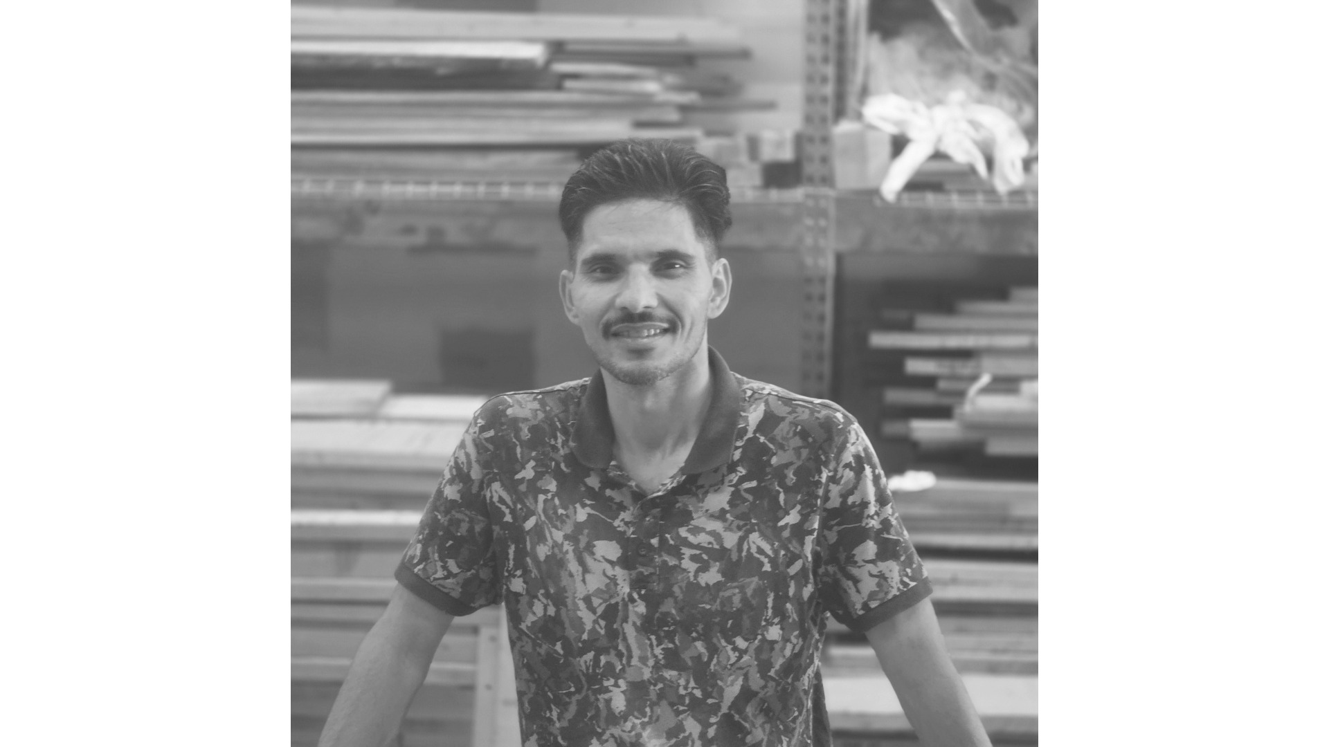 Treeboard woodworker Naqib stands at his workbench with hardwood lumber in the background.
